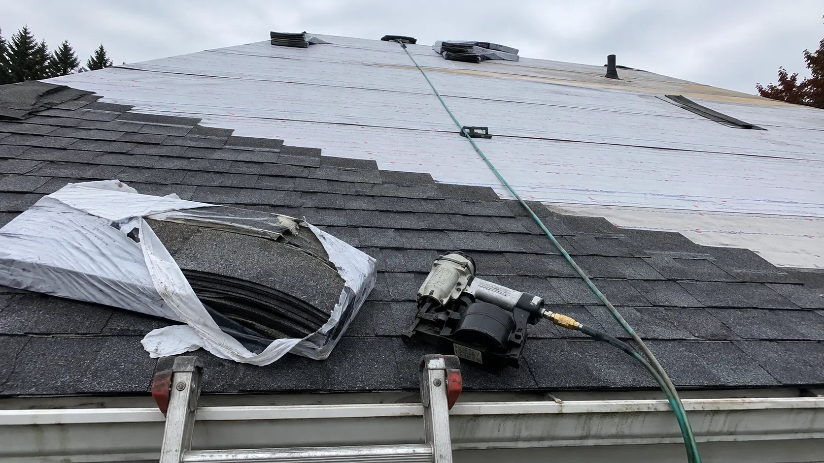 Ladder-height view of an asphalt shingle roof installation in progress
